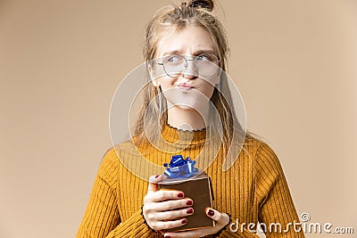 Positive Caucasian Blond Female Girl with Tiny Golden Yellow Gift Christmas Box Wearing Glasses And Holding Present Box Stock Photo