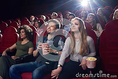 Positive couple watching funny movie at cinema and eating popcorn. Stock Photo