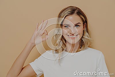 Positive cute blonde young woman in white tshirt shows OK sign with one hand Stock Photo