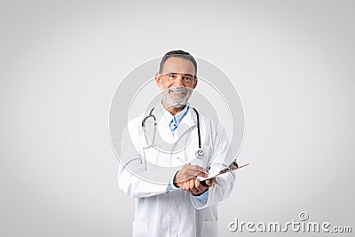 Positive european senior man doctor in white coat with stethoscope make notes, enjoy work Stock Photo