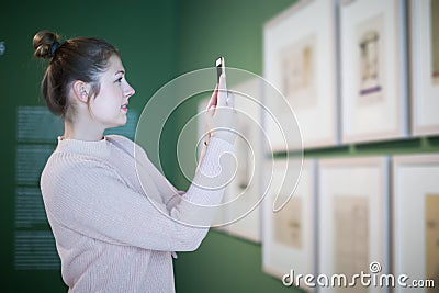 Positive female visitor with mobile standing in museum Stock Photo