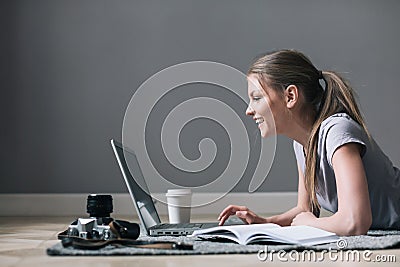 Positive girl with laptop surfing Internet, laying on the floor. Stock Photo