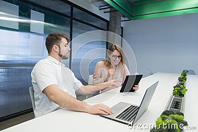 positive girl with a tablet and a man with a notebook work in the office. A man shows a woman on the tablet Stock Photo
