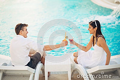 Positive happy couple having a romantic afternoon by the pool in luxury summer vacation resort.Drinking cocktails.Relaxing Stock Photo