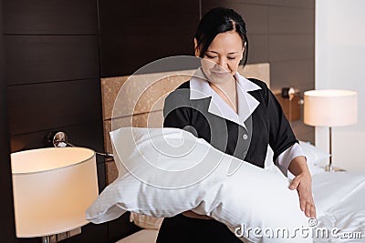 Positive hard working hotel maid looking at the pillow Stock Photo