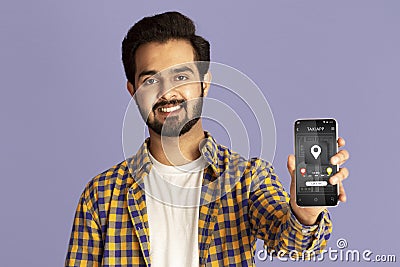 Positive Indian guy showing cellphone with online taxi service application on violet studio background Stock Photo