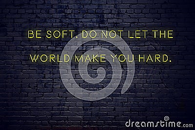 Positive inspiring quote on neon sign against brick wall be soft do not let the world make you hard Stock Photo