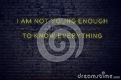 Positive inspiring quote on neon sign against brick wall i am not young enough to know everything Stock Photo