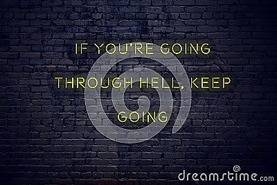 Positive inspiring quote on neon sign against brick wall if youre going through hell keep going Stock Photo