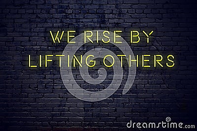 Positive inspiring quote on neon sign against brick wall we rise by lifting others Stock Photo