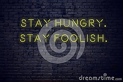 Positive inspiring quote on neon sign against brick wall stay hungry stay foolish Stock Photo