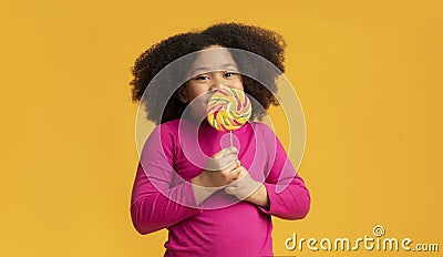 Positive little afro girl licking lollipop candy, enjoying sugar treat Stock Photo