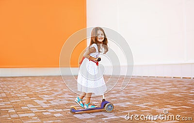 Positive little joyful girl in dress on the scooter Stock Photo