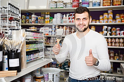 positive male customer examining various types of brushes in paint store Stock Photo