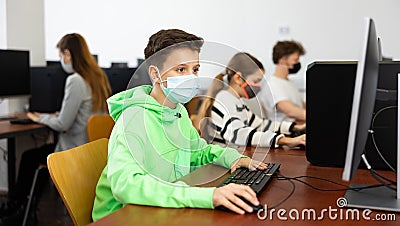 Positive male student wearing face mask working on computer in library. Concept of adult self education during pandemic Stock Photo