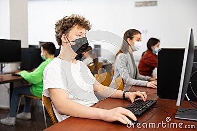 Positive male student wearing face mask working on computer in library. Concept of adult self education during pandemic Stock Photo