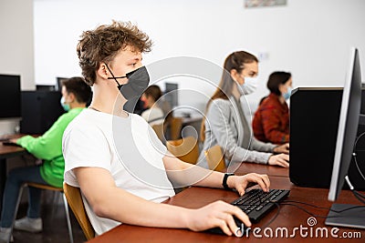 Positive male student wearing face mask working on computer in library. Concept of adult self education during pandemic Stock Photo