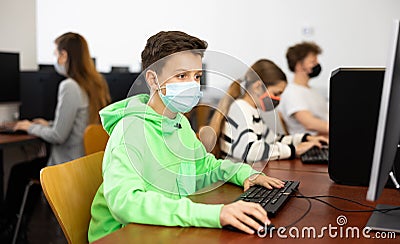 Positive male student wearing face mask working on computer in library. Concept of adult self education during pandemic Stock Photo
