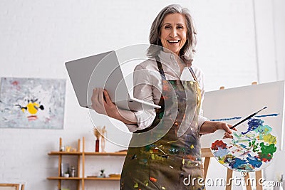 positive mature artist holding palette and Stock Photo