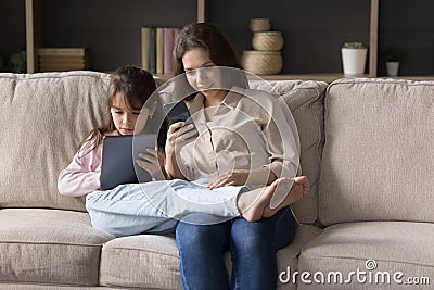 Positive mom and kid focused on gadget screens sitting close Stock Photo