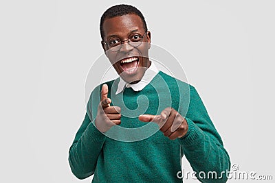 Positive overjoyed dark skinned man points at camera with both index fingers, hints on something, wears casual green Stock Photo