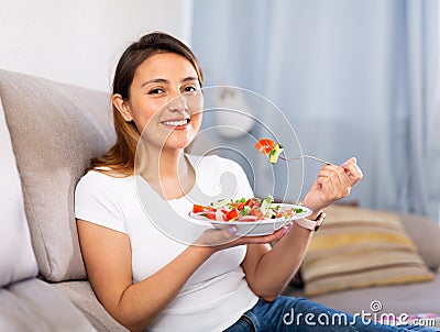 Peruvian housewoman eating vegetable salad on sofa at home Stock Photo