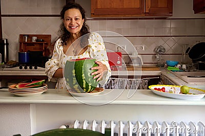 Positive pleasant housewife smiling looking at camera, slicing ripe organic juicy watermelon Stock Photo