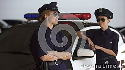 Positive police women standing near car, talking and smiling, break from work Stock Photo
