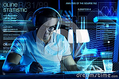 Positive programmer listening to music while making notes Stock Photo