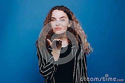 Positive romantic curly girl sending air kiss. standing over blue background. Love or romance concept Stock Photo