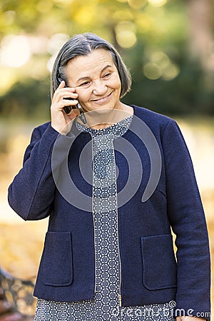 Positive senior woman talking on smartphone outdoors Stock Photo