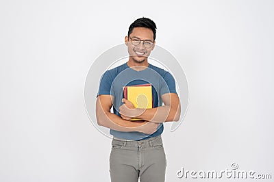 A positive, smiling Asian man is standing on an isolated white background with books in his hand Stock Photo