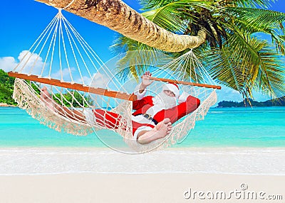 Positive smiling Christmas Santa Claus relax in hammock at island sandy ocean beach Stock Photo