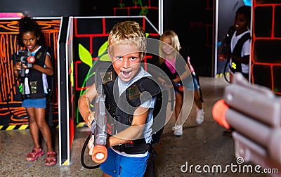 Positive teen boy standing with laser pistol in dark lasertag room during game with friends Stock Photo