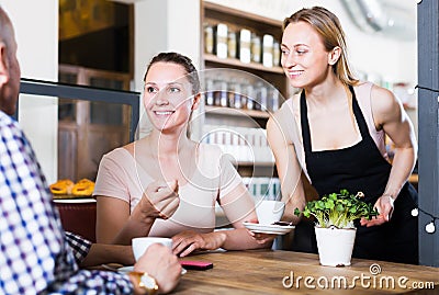 Positive waiter girl brought cup of coffee for couple of different aged people Stock Photo