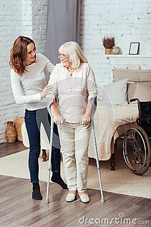 Positive woman helping he grandmother to walk with crutches Stock Photo