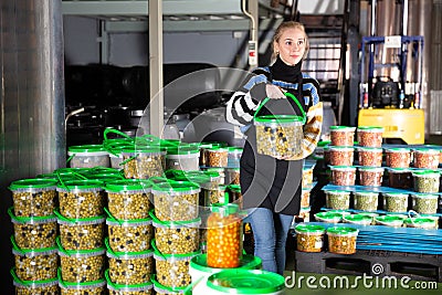 Positive woman working at the warehouse, stacking plastic containers with the selected olives Stock Photo