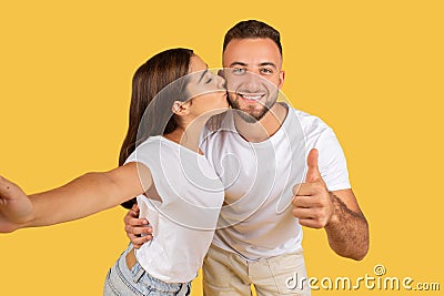 Positive young caucasian lady in white t-shirt kiss man in check, have fun, enjoy date, show thumb up Stock Photo