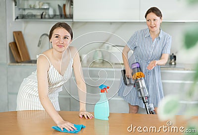 Young girl cleaning the table surface, mother vacuum-cleaning in the kitchen Stock Photo