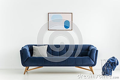 Poster above blue sofa with cushion in white living room interior with blanket in basket. Real photo Stock Photo