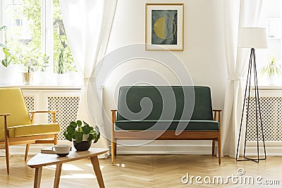 Poster above green bench between lamp and yellow armchair in vintage living room interior. Real photo Stock Photo