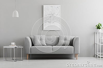 Poster above grey couch in minimal living room interior with lamp above table. Real photo Stock Photo