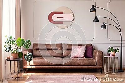 Poster above leather couch with pillows in white flat interior with plants and lamp Stock Photo