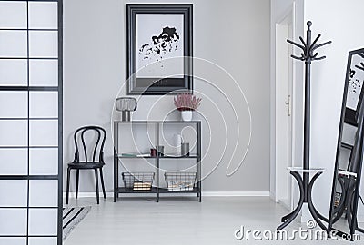 Poster above shelves with flowers and lamp in white simple hall interior with rack and black chair Stock Photo