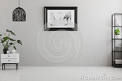 Poster on grey wall in empty living room interior with lamp above plant on cabinet. Real photo. Place for your sofa Stock Photo