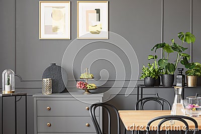 Posters above grey cabinet in dark dining room interior with plants and wooden table. Real photo Stock Photo