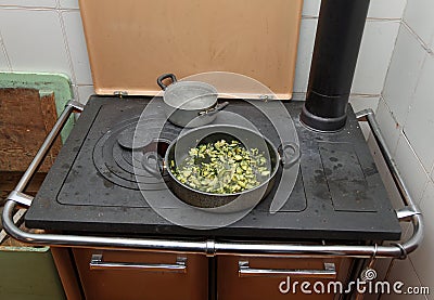 Pot with cooked zucchini in the ancient stove with fire lit Stock Photo