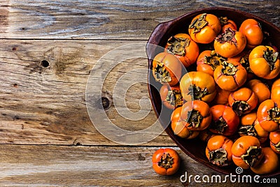 Pot of fresh fruits persimmon kaki on wooden background. Copy space Stock Photo