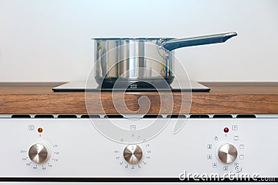 Pot ladle on induction cooker built into wood kitchen worktop view of oven knob relay Stock Photo