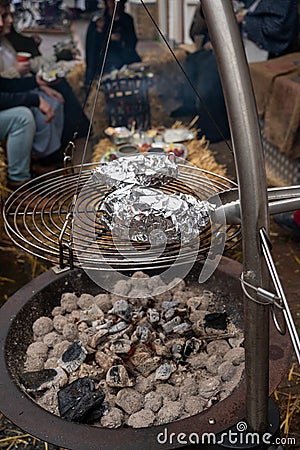 Potato in alumnium foil baked on charcoal barbecue grill outdoor Editorial Stock Photo